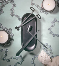 Editorial aerial shot of the tools in the center of the image against a sea foam green background surrounded by chains a statue and 2 lit candles. 